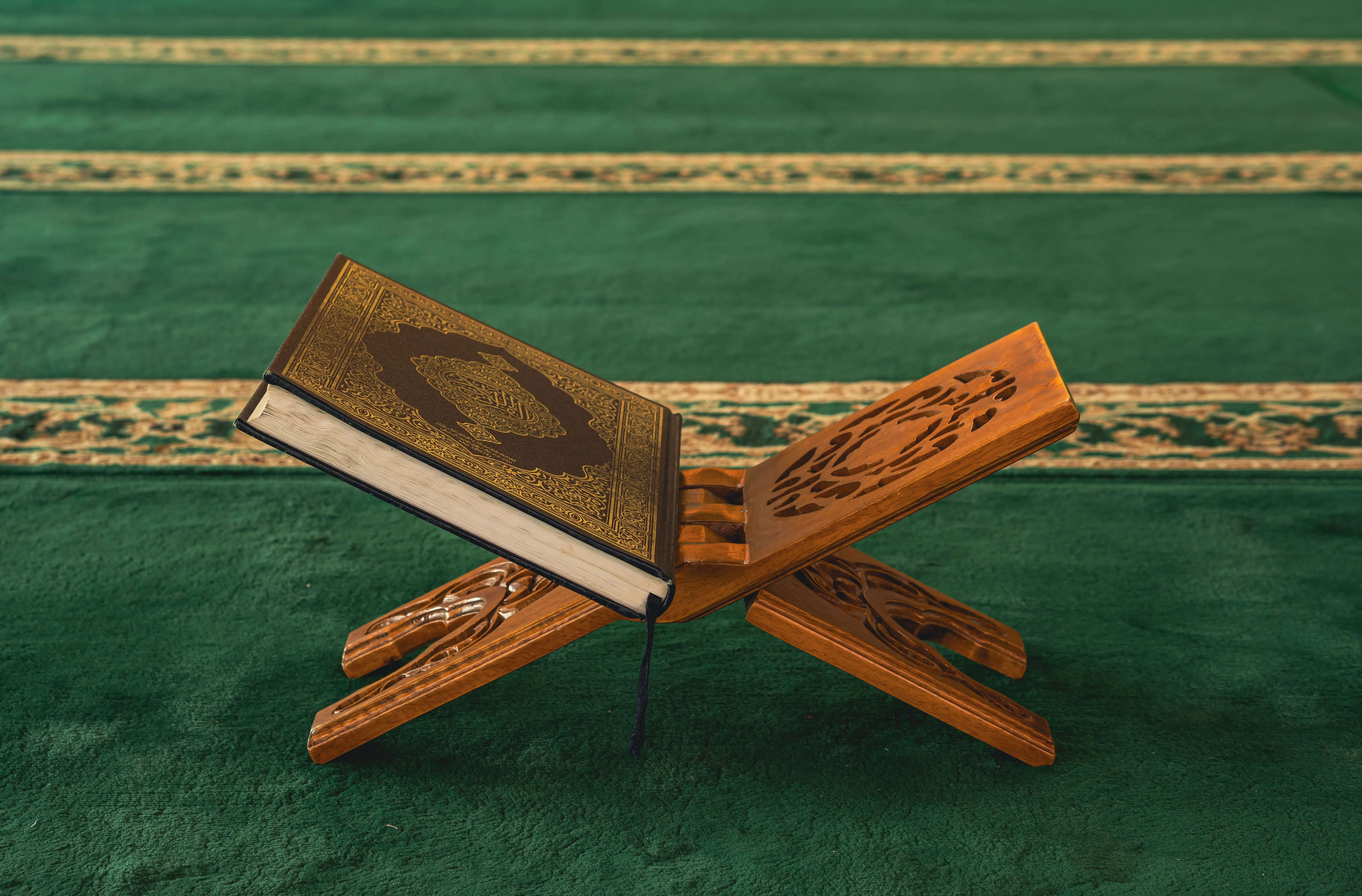 Al-Qur'an terbuka di atas rehal kayu di dalam interior masjid.